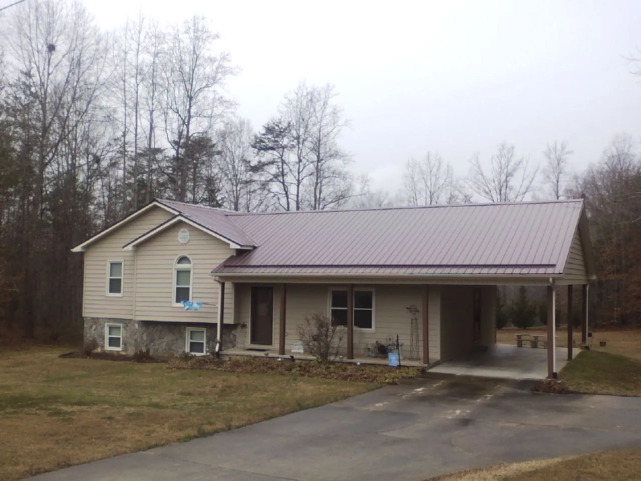 Burgundy metal roof on a tan split level home with an attached carport in Satsuma