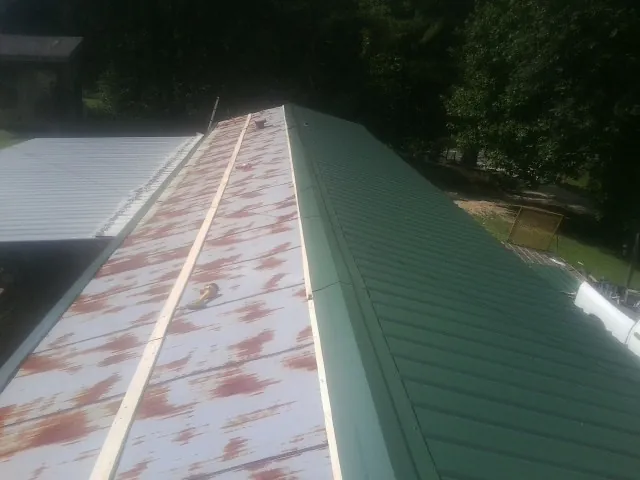 Old rusted panels beside newly installed green metal roofing — Wind Damage Roof Repair by Roofing Brothers in Satsuma