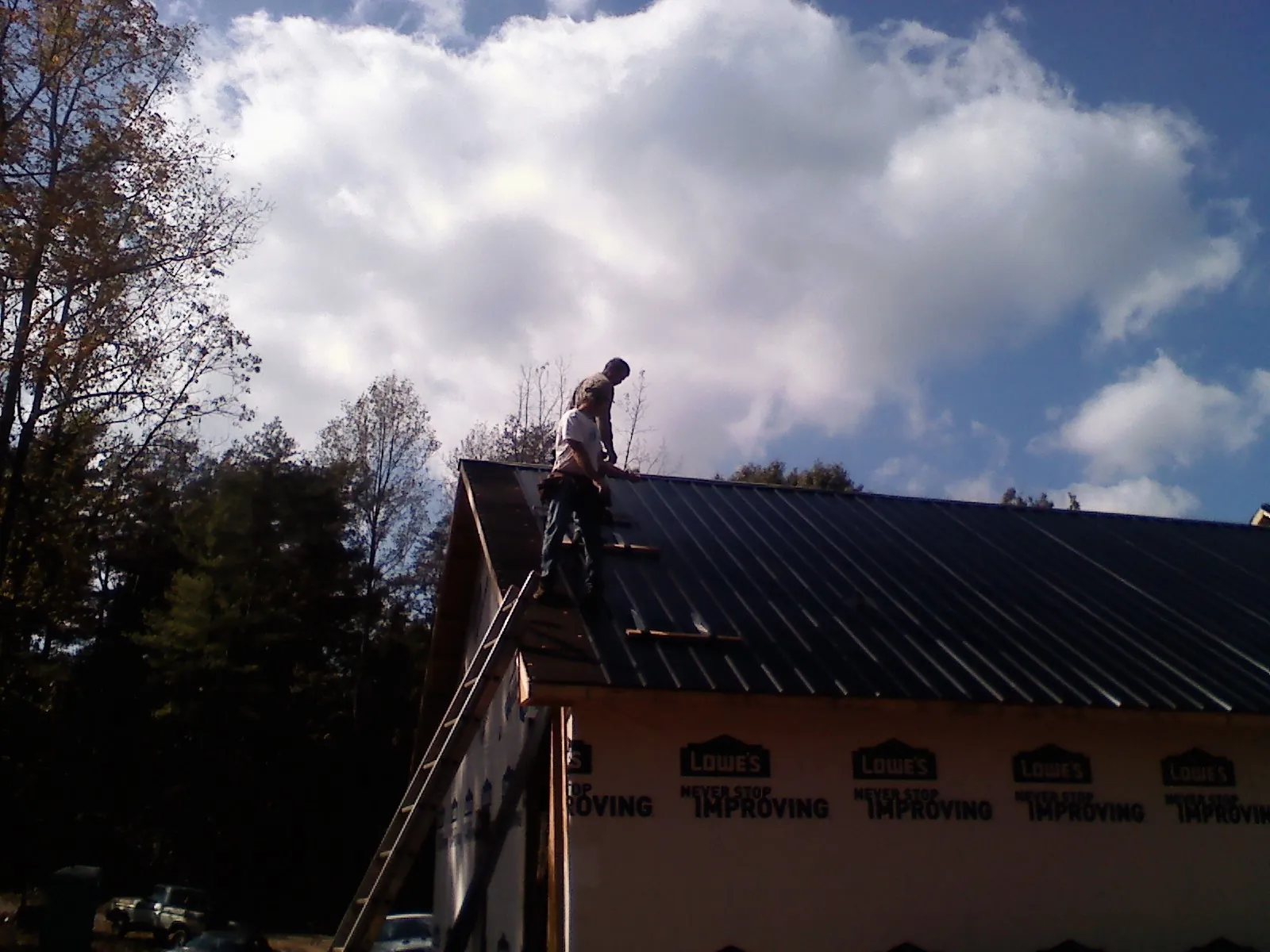 Roofer fastening dark metal panels high against a cloudy sky, from a Roof Inspection job in Satsuma