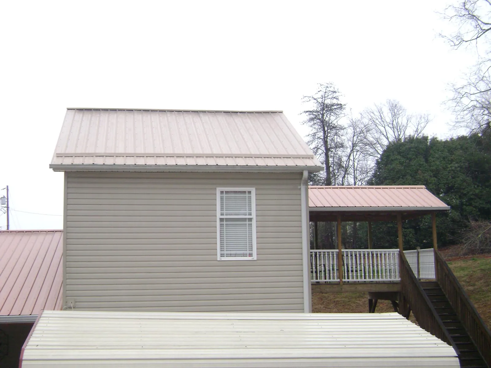 Tan metal roofs on a two story addition and attached porch, from a Roof Replacement job in Satsuma